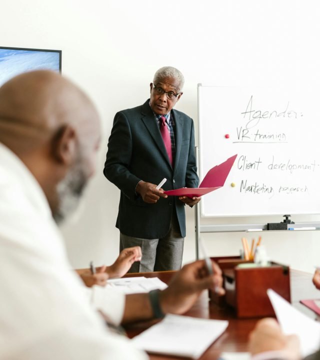 Senior businessman presenting in an office meeting with colleagues.